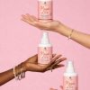 Magic Lizz – Spray lissant thermoprotecteur MYA COSMETIC – trois flacons tenus en main sur fond rose