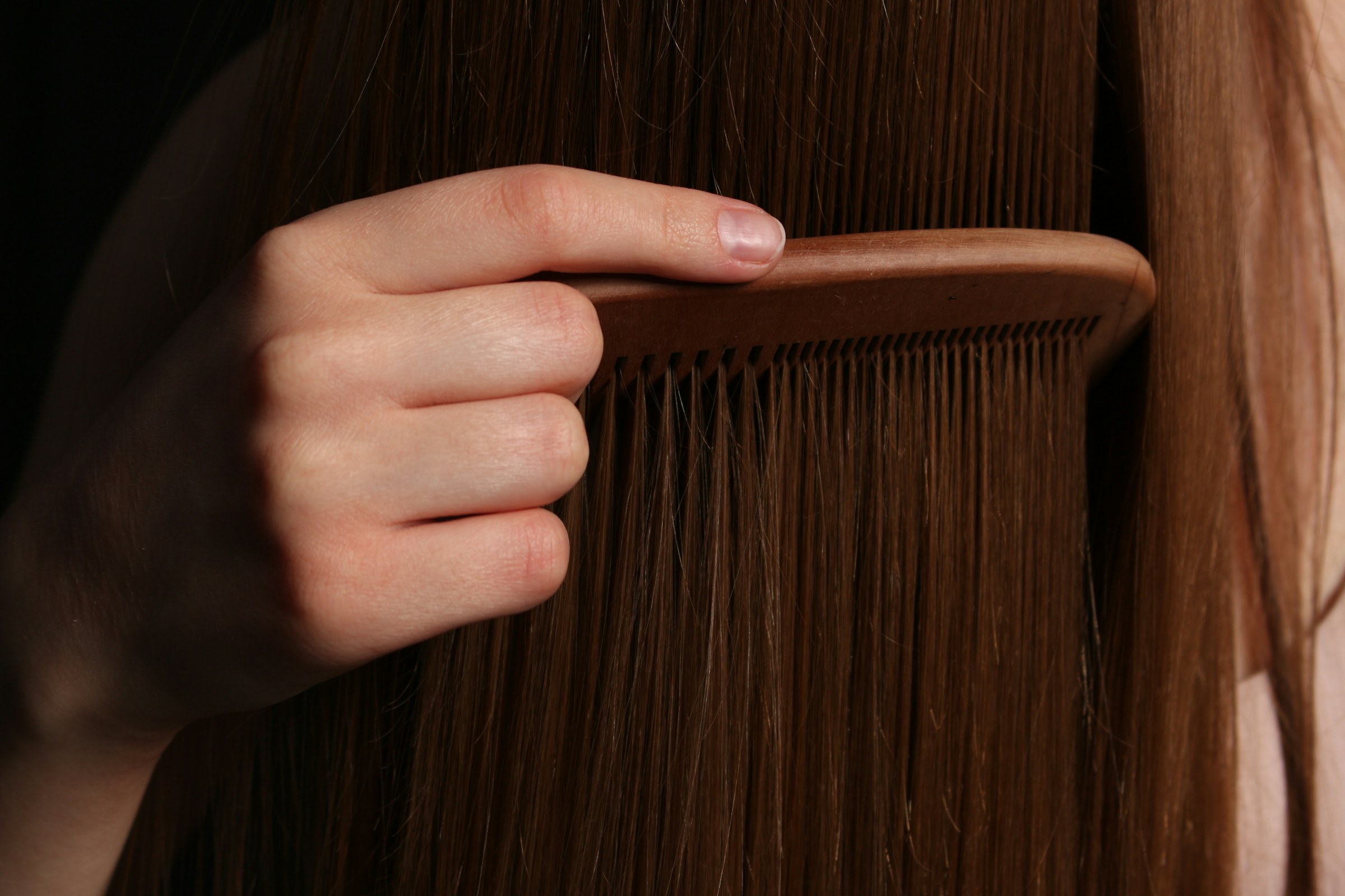 Main démêlant de longs cheveux châtains lisses avec un peigne en bois