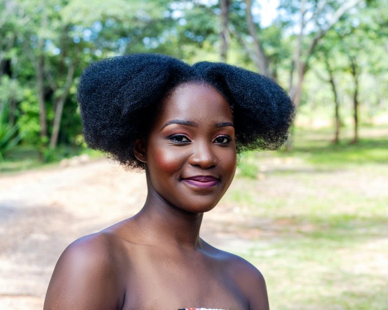 Portrait lumineux d’une jeune femme noire souriante aux cheveux crépus volumineux, en plein air