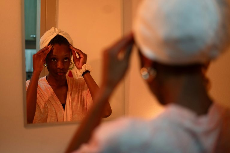 Femme en peignoir ajustant une serviette sur ses cheveux devant un miroir, dans une lumière chaude