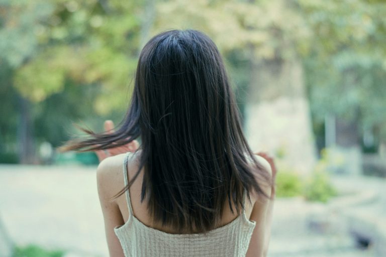 Femme de dos aux cheveux bruns lisses et brillants, dans un parc ensoleillé