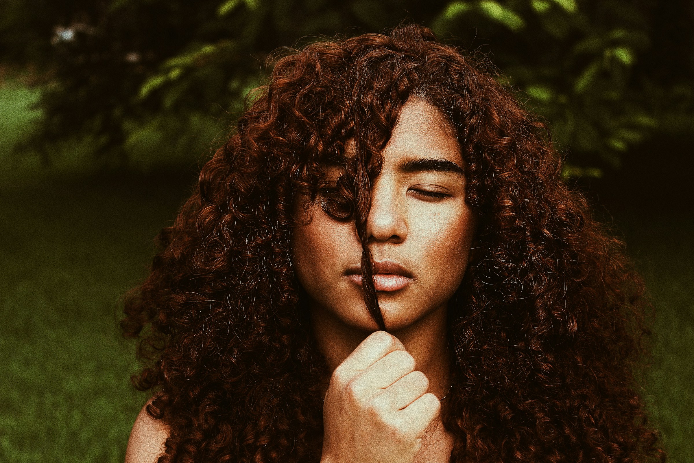 Femme aux longues boucles définies brun cuivré, une mèche tenue devant le visage, lumière naturelle