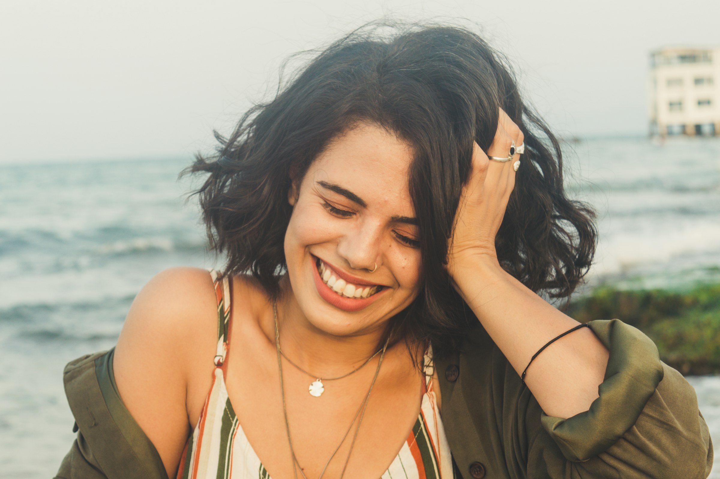 Femme souriante aux cheveux bruns ondulés, la main posée dans ses cheveux, en lumière douce